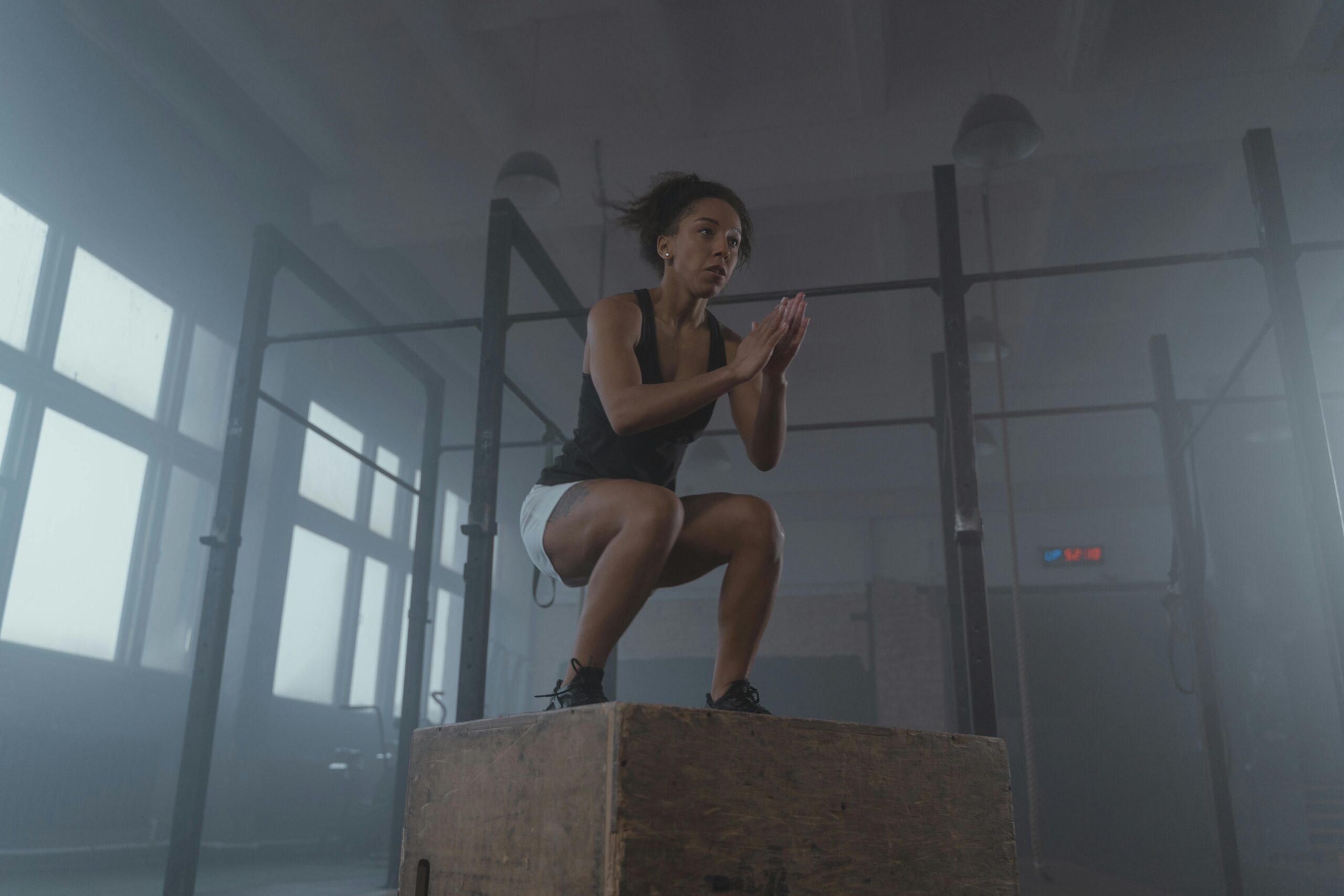 A determined woman executing a box jump in an indoor gym setting, showcasing strength and fitness.