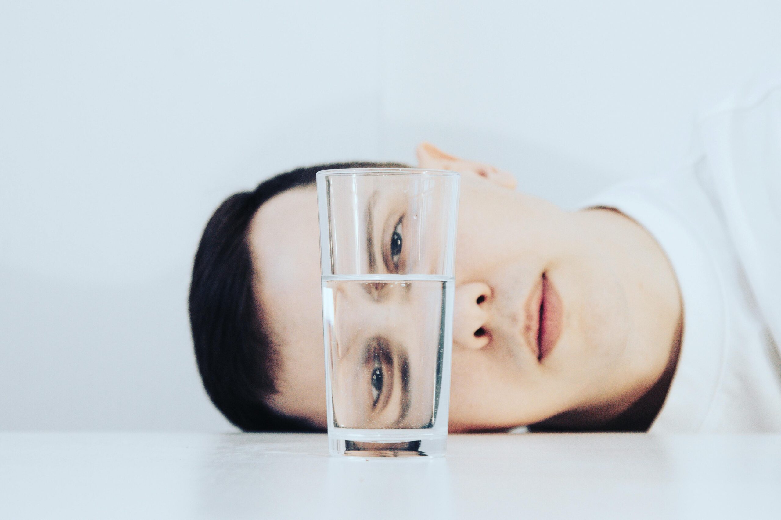 Close-up view of a man lying beside a glass of water with a unique perspective.
